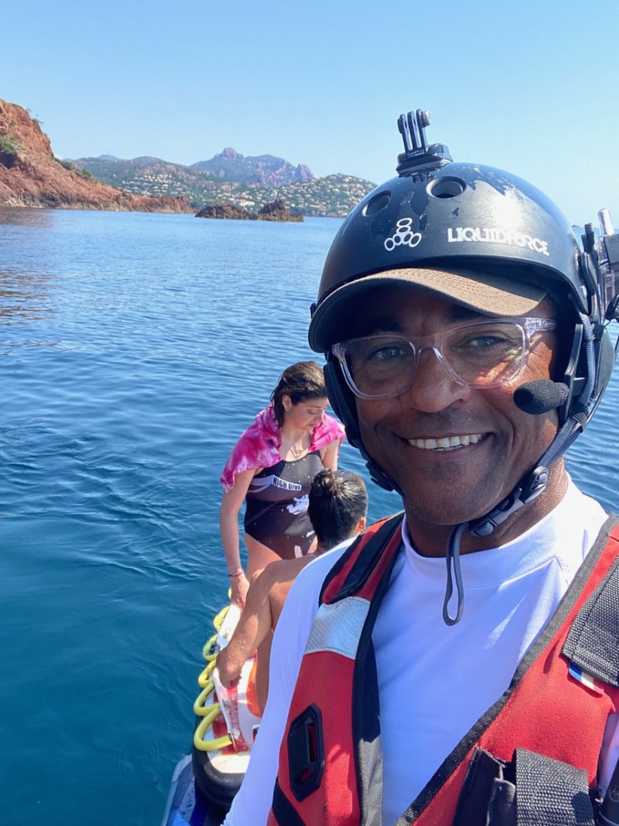 Homme souriant avec casque Liquid Force et gilet de sauvetage lors d'une activité nautique en mer.