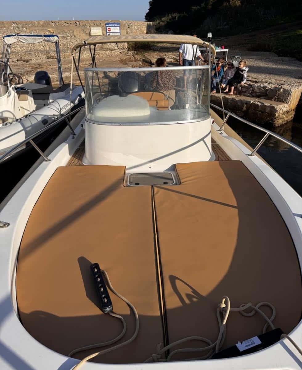 Pont avant d'un bateau à moteur avec bains de soleil marron, vue sur la console et le quai ensoleillé au port.