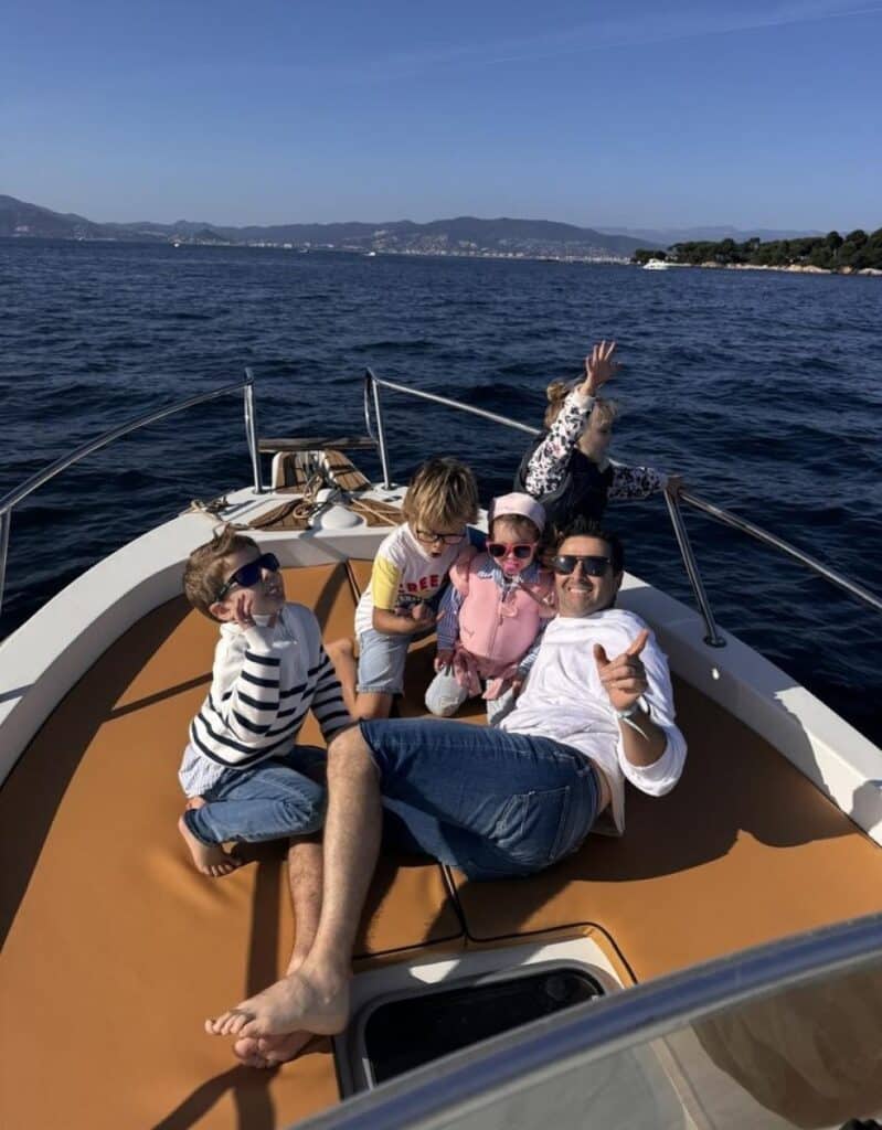 Sortie en Famille en Bateau : Vacances d'Été en Mer Famille joyeuse sur le pont d'un bateau en mer, profitant d'une sortie ensoleillée avec vue sur les montagnes.