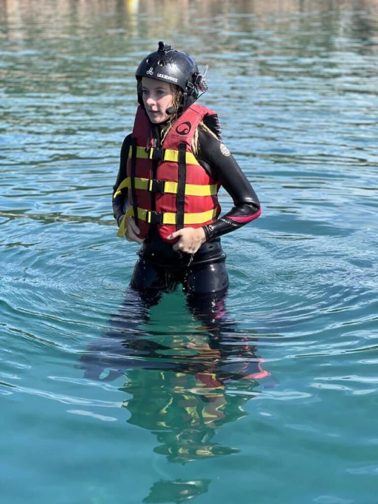 Femme en combinaison et casque Liquid Force portant un gilet de sauvetage rouge et jaune dans l'eau.