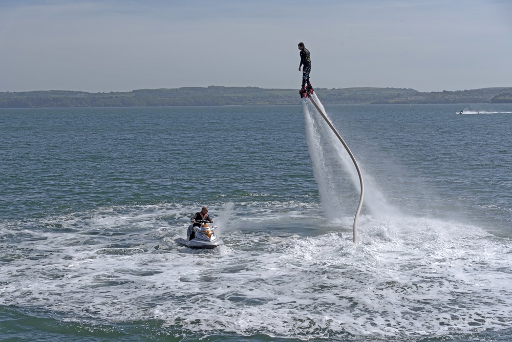 Flyboard et Jet Ski : Spectacle de Voltige Nautique en Mer Homme en flyboard s'élevant au-dessus de la mer relié à un jet ski, sport nautique acrobatique.