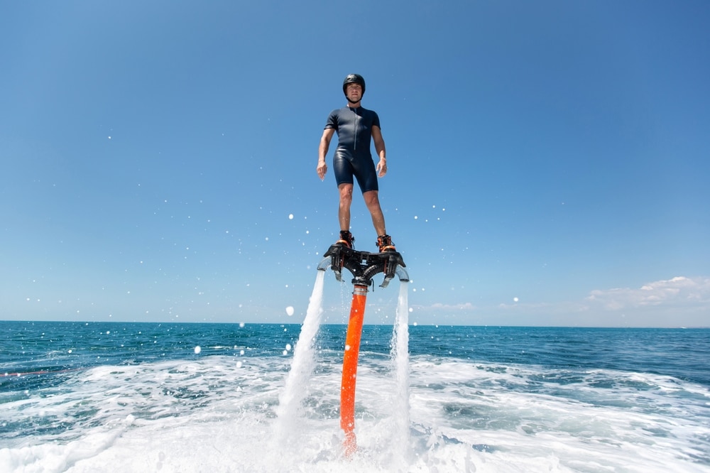Flyboard au-dessus de l'océan : sport nautique extrême Homme en flyboard propulsé par des jets d'eau au-dessus d'une mer bleue, sensations fortes et sport nautique.