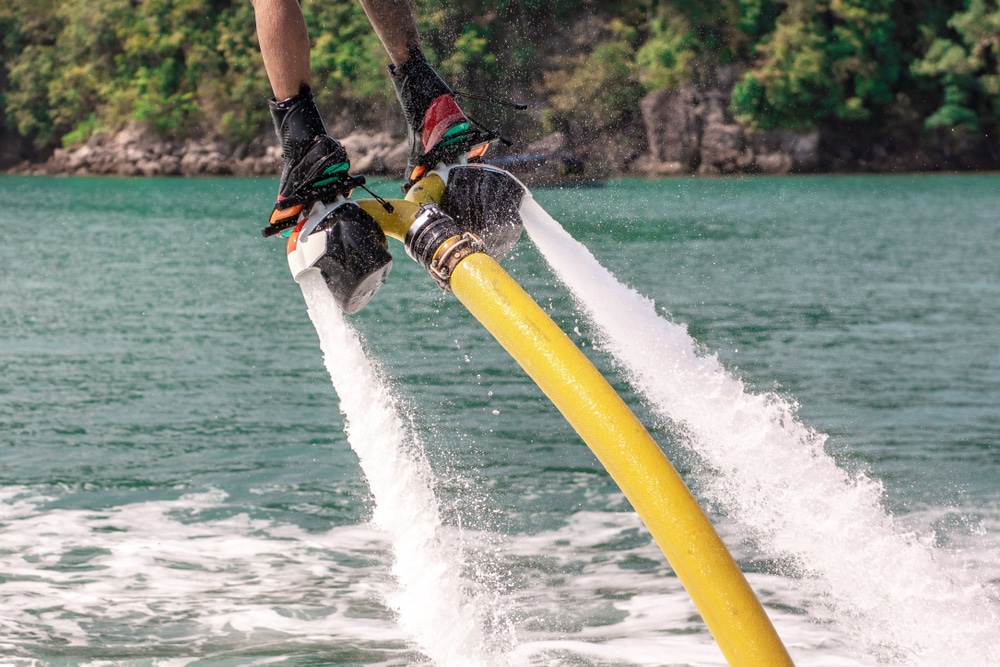 Expérience Flyboard Intense au-dessus de l'Eau Turquoise Flyboarder propulsé par des jets d'eau puissants au-dessus de la mer turquoise près d'une côte boisée.