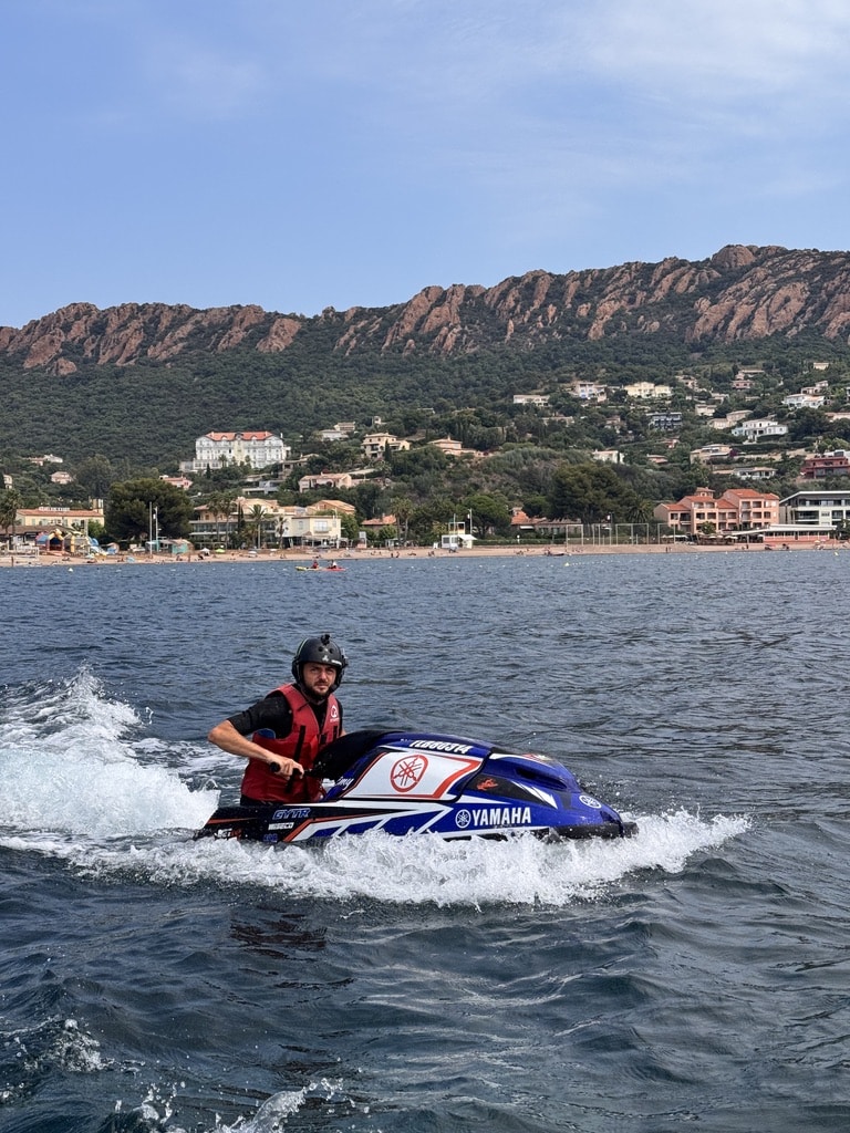 Jet Ski Yamaha en Mer : Aventure sur la Côte d'Azur Homme sur un jet ski Yamaha bleu avec vagues, massif de l'Estérel et plage en arrière-plan.