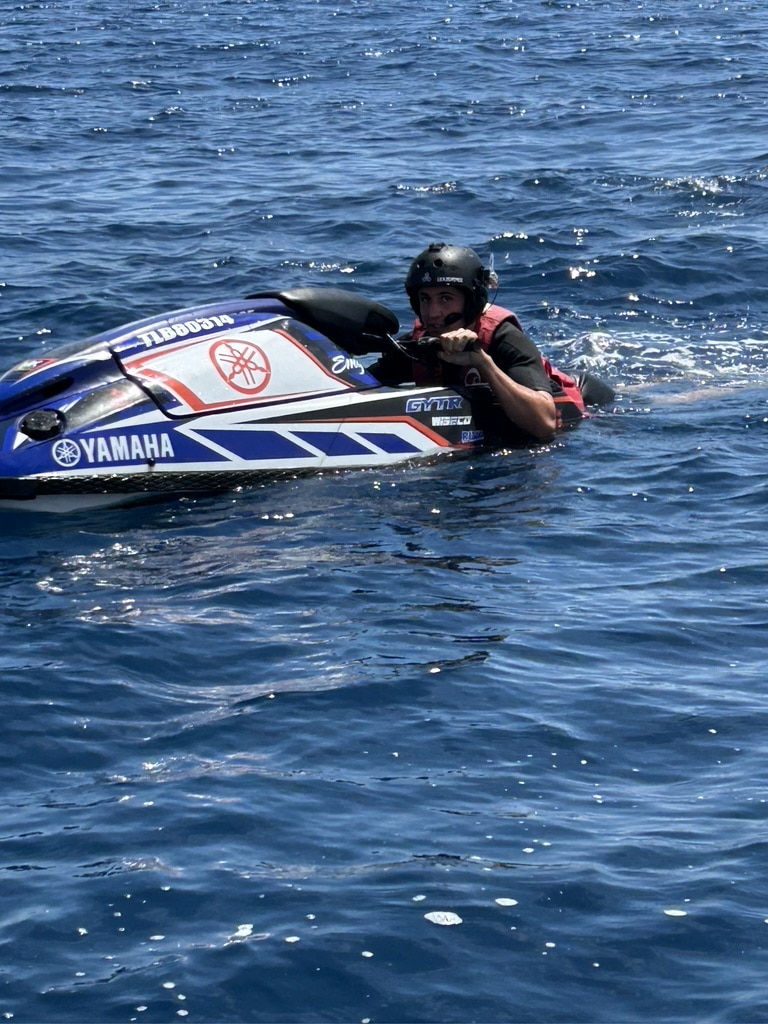 Jet ski Yamaha en mer avec pilote équipé d'un casque Homme avec casque et gilet rouge sur un jet ski Yamaha bleu et blanc (TLBB0314) dans la mer bleue.