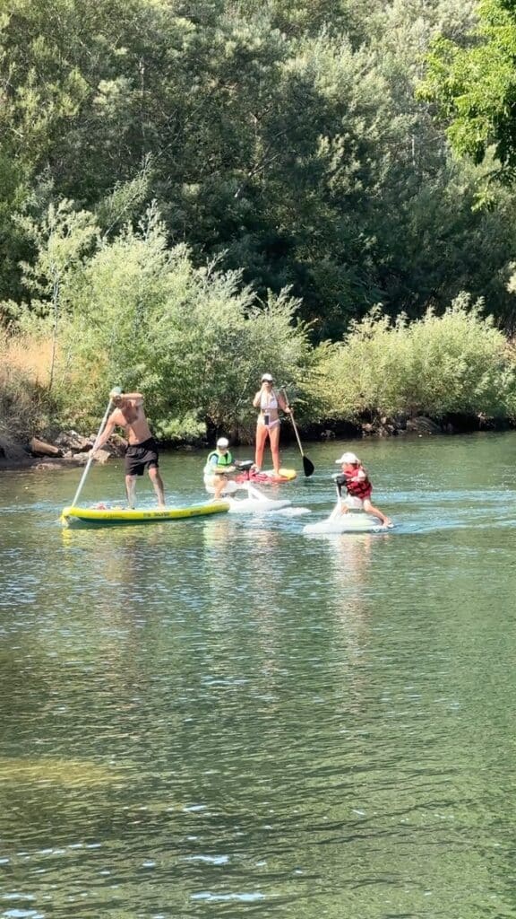 Paddleboard et Activités Nautiques en Famille sur Rivière Famille pratiquant le paddle et le scooter des mers électrique sur une rivière calme bordée de végétation dense.