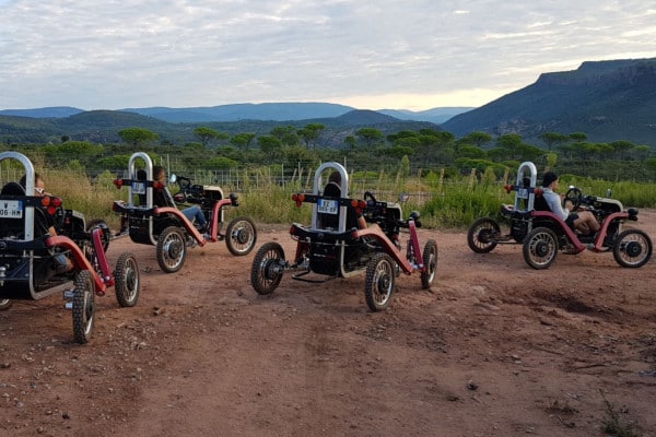 Groupe en randonnée buggy tout-terrain sur un chemin de terre face aux montagnes au coucher du soleil.