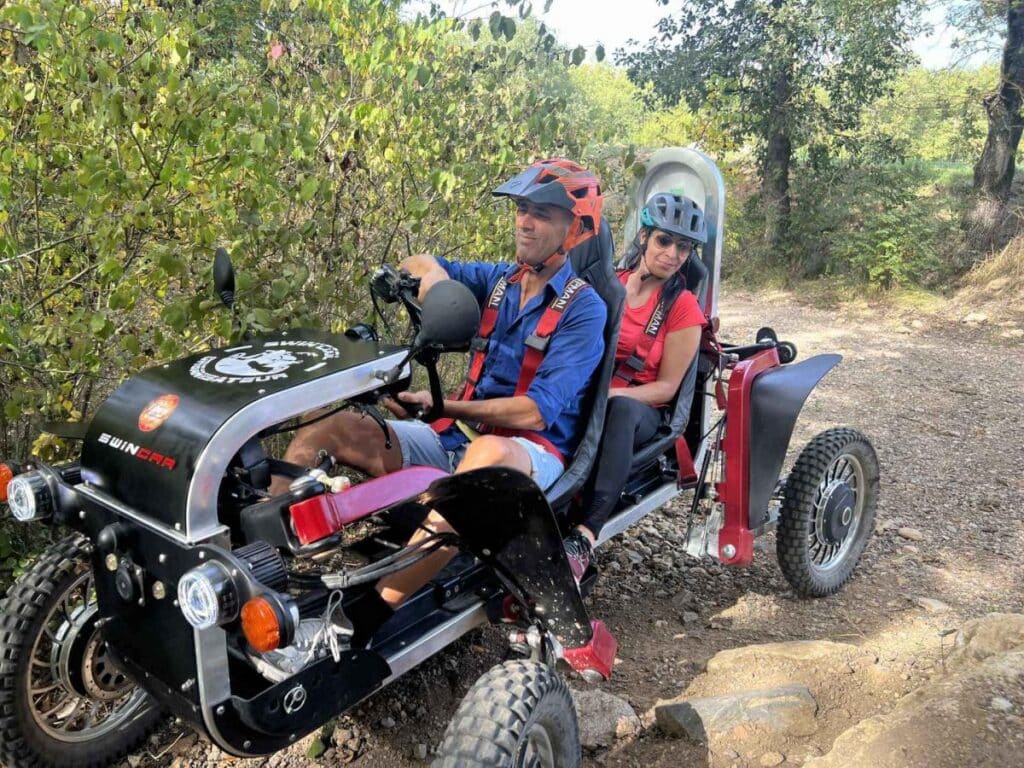 Couple souriant pilotant un Swincar tout-terrain sur un sentier forestier accidenté.