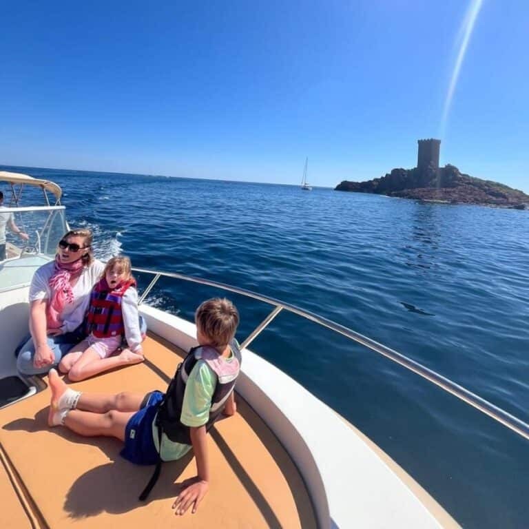 Balade en bateau devant l'Île d'Or à Saint-Raphaël Famille en bateau devant la tour de l'Île d'Or à Saint-Raphaël, navigation en mer sous un soleil radieux.