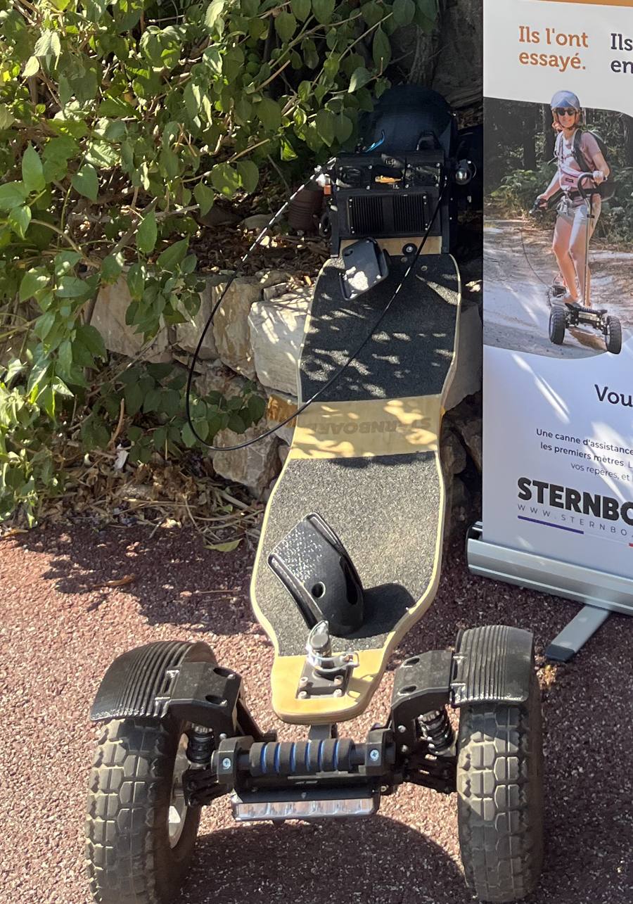 Skateboard électrique tout terrain Sternboard avec suspensions et pneus larges devant un panneau publicitaire.